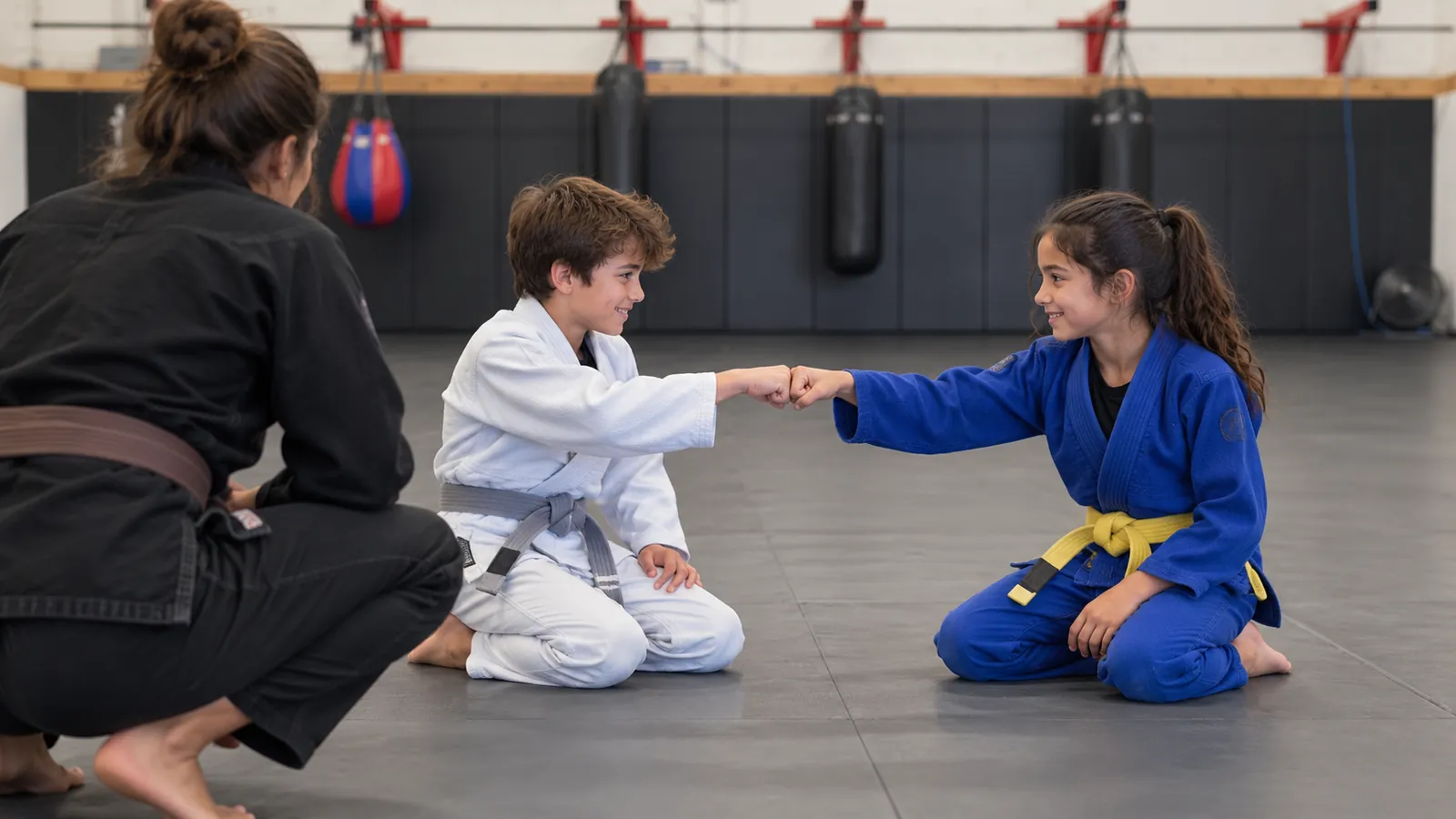 Two children bump fists before a round as their coach looks on